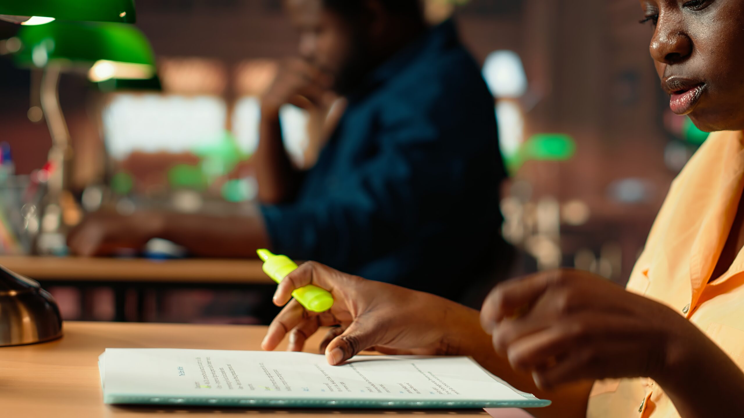 African american scholar highlighting the relevant information from class notes, creating a summary with highlighter pen. Student underlining key words and phrases from the course. Camera B.