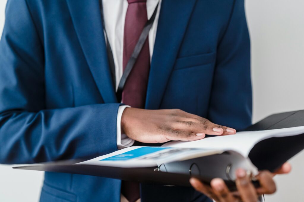 Close-up of a businessman in a suit reviewing a binder in a professional setting.